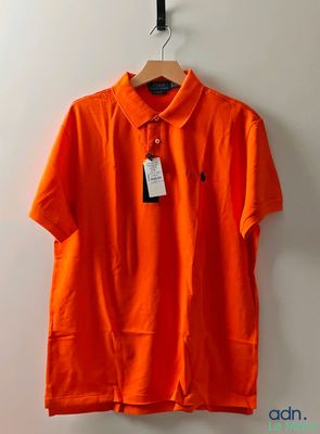 un polo orange suspendu à un cintre accroché au mur