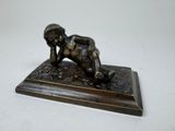 bronze figurine of a boy laying on his stomach on a wooden base