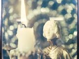une photo représentant une bougie et une statue devant un sapin de Noël