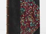 an old book with a floral design on it sitting on a white surface