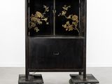 a black cabinet with gold flowers and wheels on a concrete floor
