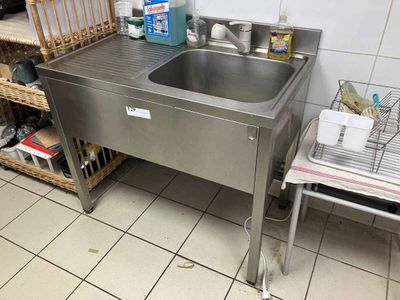 a stainless steel sink in a kitchen with a wire basket on the floor