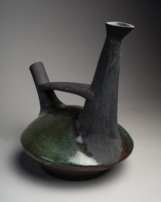 un vase noir et vert posé sur une surface blanche