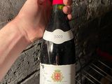 a person holding a bottle of wine in front of a brick wall