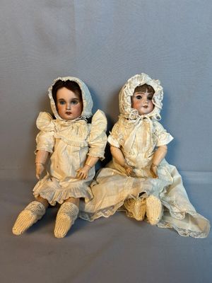 une paire de poupées anciennes en porcelaine assises l’une à côté de l’autre sur une surface grise
