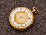 une montre de poche en or avec un cadran blanc sur un fond marron