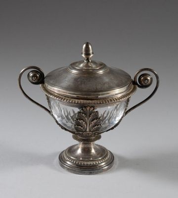 une tasse plaquée argent avec un couvercle en verre, posée sur un socle
