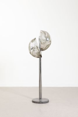 sculpture représentant trois fleurs en argent posée sur un socle métallique devant un mur blanc