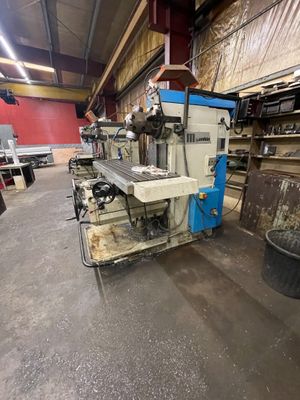 Une grande machine est entreposée dans un entrepôt, à côté d'autres machines.