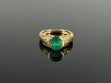 an emerald and diamond ring on a reflective surface