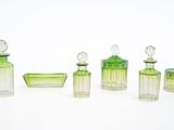 quatre flacons de parfum en verre vert et un bol en verre posés sur une surface blanche