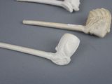 three white porcelain pipe holders with carved heads on a gray surface