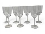 six empty wine glasses lined up in a row on a white surface