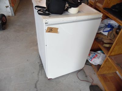 un réfrigérateur blanc posé dans un garage, avec un sac posé dessus