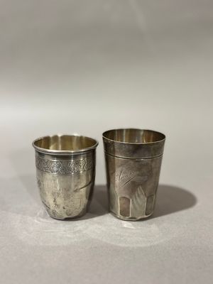 paire de verres à shot anciens en métal argenté, posés sur une surface blanche