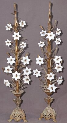 une paire de fleurs blanches posées sur des bougeoirs en métal doré, sur fond gris