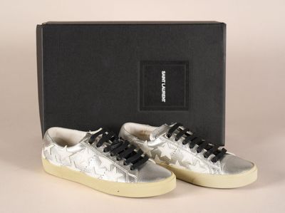 des baskets argentées avec des lacets noirs, posées devant une boîte noire