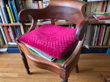 une chaise en bois avec un coussin rose devant une bibliothèque