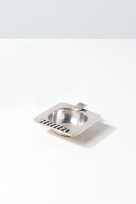 a metal ashtray on a white table with a spoon in it