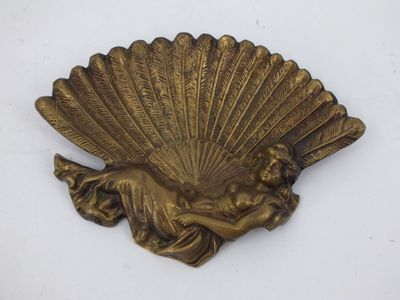 une image représentant une plaque en laiton sur laquelle figure une dame tenant un éventail