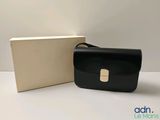 Le sac noir se trouve à côté de la boîte, sur la table.