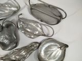 several silver metal leaf shaped purses on a white surface