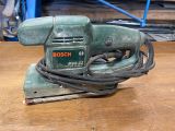 a green electric sander sitting on a wooden table