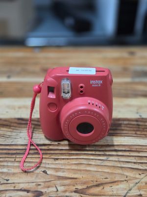 a pink camera on a wooden table with a red cord