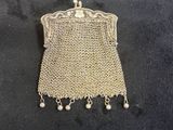 a silver mesh purse with pearls hanging from it on a black surface