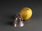 a silver bell next to an apple on a black surface