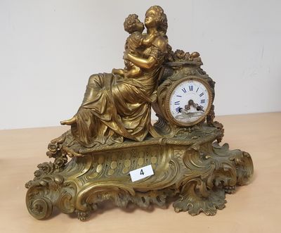 une horloge en or posée sur une table, à côté d'une femme tenant un bébé dans ses bras