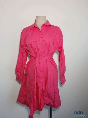 une robe-chemise rose posée sur un mannequin contre un mur blanc