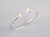 a silver cuff bracelet with two white pearls on a white background