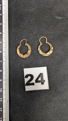 deux paires de boucles d'oreilles créoles en or posées sur une surface noire, à côté d'une règle