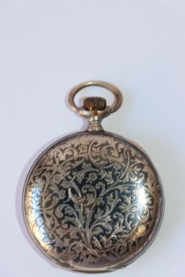 une montre de poche en argent posée sur une surface blanche
