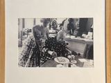 photographie en noir et blanc d'une femme assise à une table, avec une assiette de nourriture devant elle