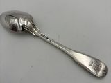 une cuillère ancienne en argent dont le manche repose sur une surface blanche