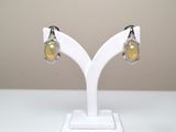 une paire de boucles d'oreilles en oplite jaune et diamants, posée sur un socle blanc