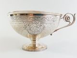 a silver bowl with a handle on a white surface