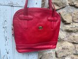 un sac à main en cuir rouge accroché à un mur de pierre, devant un mur de pierre