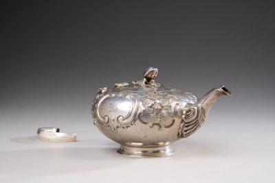 a silver teapot sitting on a table next to a ring