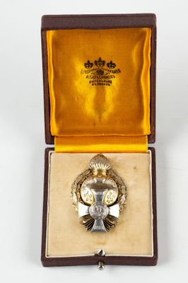 une image représentant une broche en argent dans un écrin en or, posée sur une surface blanche