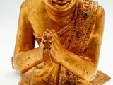 gold statue of a person sitting on the ground with his hands clasped