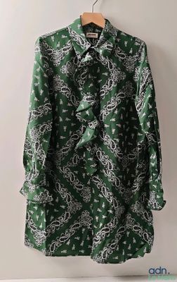 une chemise à motifs cachemire verts et blancs suspendue à un cintre devant un mur blanc
