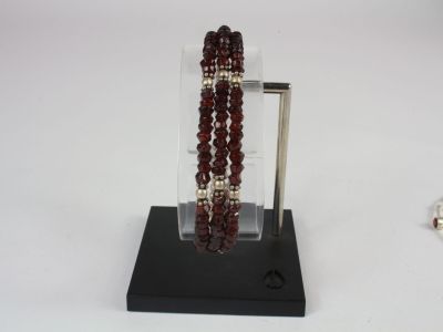 bracelet and bracelet stand on a white surface with a red beaded bracelet