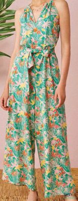 une femme debout devant une plante, vêtue d'une combinaison verte à motifs floraux