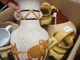 a person holding a vase in a box full of pottery