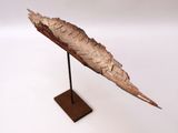 a sculpture of a leaf on a stand on a white surface