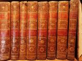 several old books are lined up in a row on a shelf