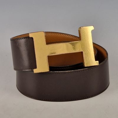 La ceinture est dotée d'une boucle en forme de « H » dorée et est en cuir marron avec une boucle dorée.